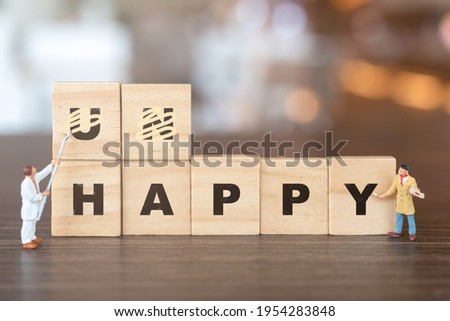 Miniature  people worker team on Unhappy word in wooden alphabet letters with prefix un crossed out, leaving the word Happy Royalty-Free Stock Photo #1954283848
