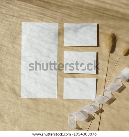 Card mockup with copy space top view.Still life composition, flat lay. Greetings, wedding invitations blank, ribbon and dry plant with sunlight shadow on beige background.  