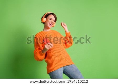 Photo of happy charming excited young woman raise fist hold phone wear headphones isolated on green color background