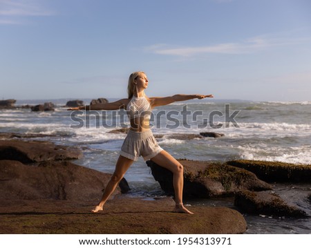 Young woman practicing yoga. Standing in Virabhadrasana II pose, Warrior II Pose. Work out. Healthy lifestyle. Strong body. Ocean background. Yoga retreat. Self-care concept. Beach in Bali, Indonesia