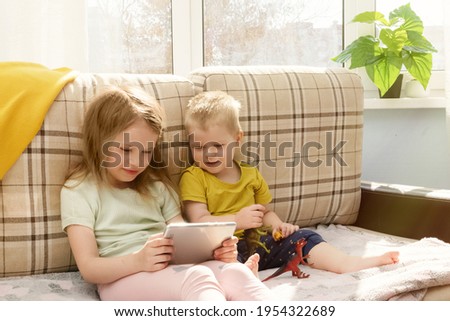 Little kids siblings seated on sofa in living room and they communicate by video holding smartphones or watch cartoon. Parental control on the internet.