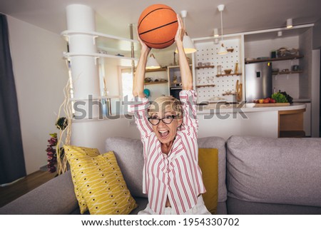 Elderly woman emotionally watching basketball on tv and celebrating victory at home.