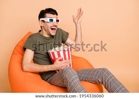 Full size photo of young happy excited man in 3d glasses sit chair eat popcorn watch cinema isolated on beige color background