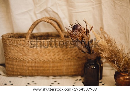 Dry protea flower in vase, pampas grass, wicker basket on boho rug on background of beige linen cloth. Atmospheric bohemian style room details. Boho decor for wedding or in studio