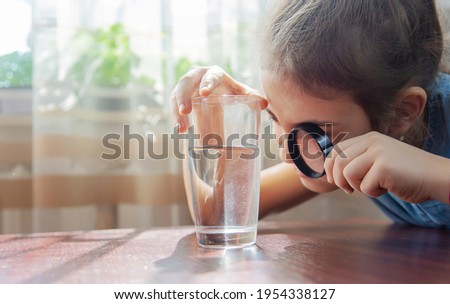 The child examines the water with a magnifying glass in a glass. Selective focus. Kid. Royalty-Free Stock Photo #1954338127