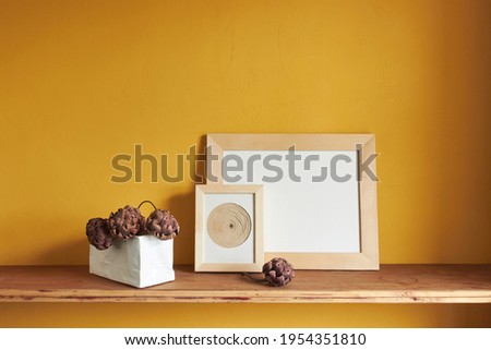 Wooden frames mockup. Dry decorative artichokes in a vase on an old wooden shelf. Composition on a yellow wall background