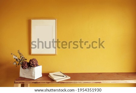 Wooden picture frame mockup. Flowerpot on a pile of books on an old wooden shelf. Composition on a yellow wall background