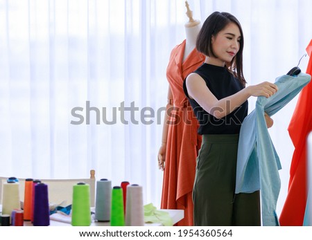 Smiling Asian woman seams  stress choose a sample of dress for sewing clothes. Fashion designer standing in clothing In order to prepair, service for customers. Concept Profession Dressmaker designer