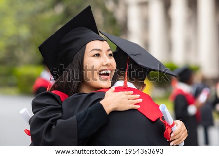 Cheerful young asian lady hugging her boyfriend while graduation ceremony at university campus. Two happy multiracial students greeting each other with successful graduation, closeup, copy space