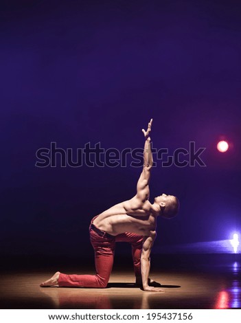Young and muscular man performing a contemporary dance pose on a stage.