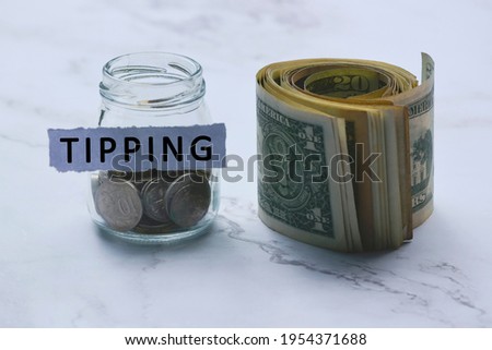 Tipping text on white torn paper with coins in a glass jar and US dollar bills