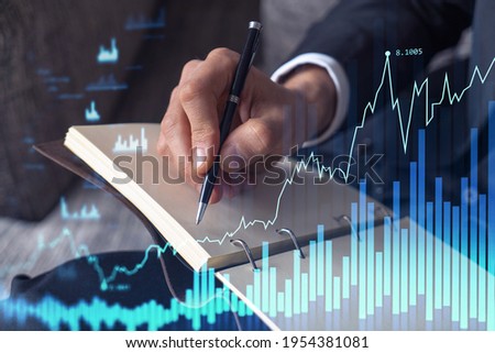 A trader in formal wear writing down some ideas to research stock market to proceed right investment solutions. Wealth management concept. Hologram Forex chart over close up shot.