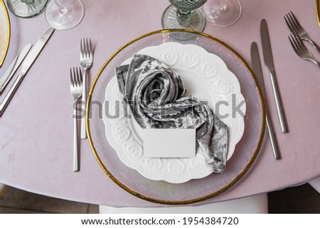 Name plate mockup with empty blank space card laying on the table decorated for wedding banquet in restaurant. Elegant modern invitation card template for the inscription of the guest on a white plate