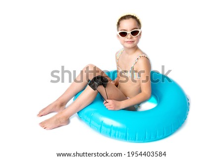 Happy little girl, in a beach suit and on an inflatable ring, takes off her protective medical black mask from her face outdoors. Studio white background. The concept of defeating the coronavirus.