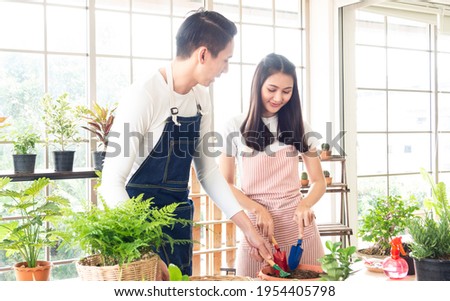 Portrait man and beautiful young woman smiling Asian bastard Thai-Chinese wearing white T-shirt and apron together decorate small tree on wooden table in stained glass room White happy relaxed bright.