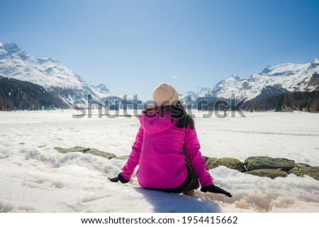 winter outdoors lifestyle portrait of young happy and attractive woman enjoying the view sitting on snow at beautiful alpine mountain during Christmas holiday