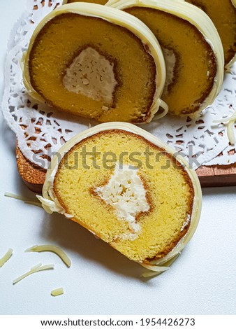 Close up view of cheese roll sponge with cheese dressing on the outside and inside in selective focus on white wooden table background