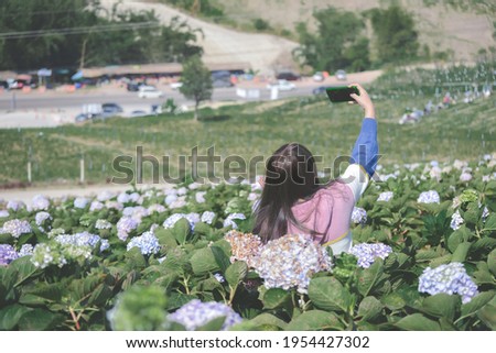 Young woman is smiling and happy in hydrangea garden.  Woman take selfie photo on cellphone in flower field
