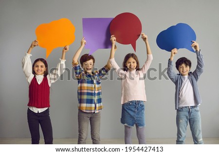 New generation voicing out opinions. Team of happy school children showing colorful speech balloon paper cards. Smiling little kids holding empty thought bubble placards standing together in studio