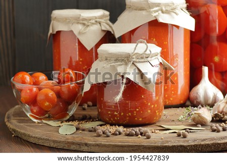 Canned homemade tomato paste and pickled tomatoes in plastic free jars on rustic table in pantry, closeup, simple living aesthetics, home storage solution, saving leftovers, canning concept