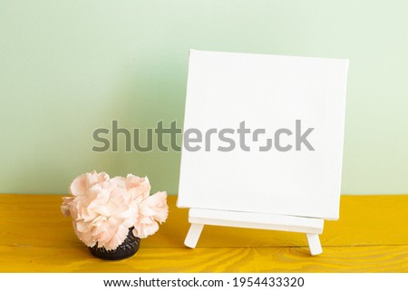 Blank white canvas with carnation flowers on wooden table. green background