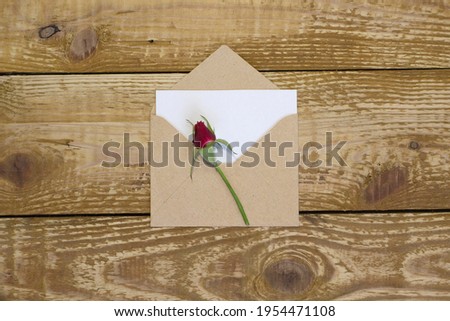 Simple small envelope with space for writing and cute small rose on wooden background with a pen close-up Narrow focus line, shallow depth of field high angle view