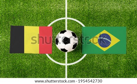 Top view ball with Belgium vs. Brazil flags match on green football field.
