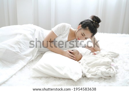 Mother in white dress gentlely pat her baby with warm and calm and lulling her to nice sleep on white bed. Mom activity with chid, bonding betweeen family.