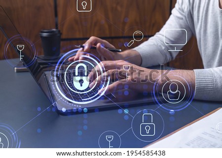 A programmer is typing a code on a keyboard to protect a cyber security from hacker attacks and save clients confidential data. Padlock Hologram icons over the typing hands. Royalty-Free Stock Photo #1954585438