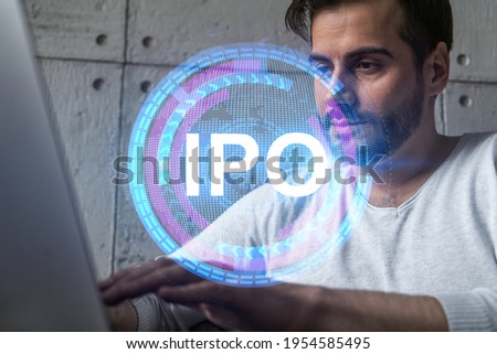 A serious caucasian analyst in casual wears, using laptop to analyze the profit of IPO project. Double exposure. Initial public offering Hologram. Concept of a growth of investments.