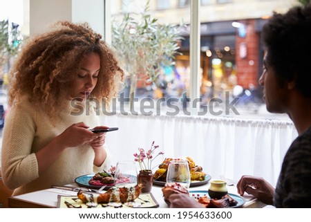 Food blogger taking picture of meal in restaurant on mobile