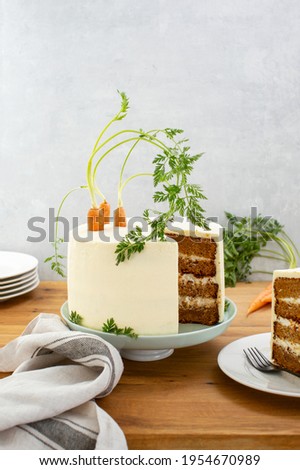 Old fashioned recipe spiced moist carrot cake with cream cheese frosting, decorated with fresh carrots, front view