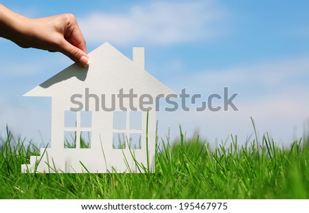 Paper house in green grass over blue sky. Concept of construction or mortgage. Eco