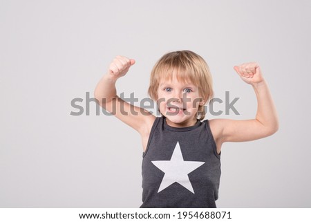 Caucasian child in a black and white T-shirt with star made gesture with his hands, showing super power, muscle. Portrait of cheerful boy. Childhood, growing up, kid's health concept. Copy space.