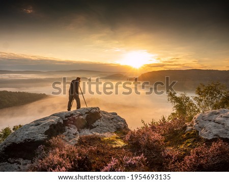 Landscape photographer in action taking picture. Silhouette man photographing against misty landscape and morning sky. Autumn colorful sunset
