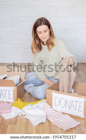 Young woman sitting on floor and packing clothes in cartoon box for donations.