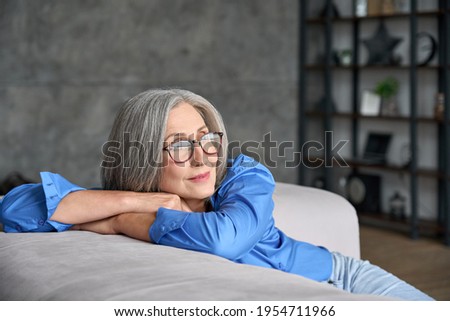 Mature peaceful 60s middle age lady sitting relaxing at home. Senior elder serene woman in glasses looking at window thinking of positive vision, dreaming of future and enjoying wellbeing. Royalty-Free Stock Photo #1954711966