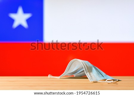 A medical mask lies on the table against the background of the Chilean flag. The concept of a mandatory mask regime for residents of the country and tourists in Chile during a pandemic.