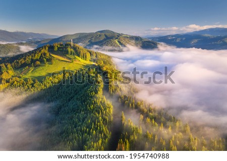 Mountains in clouds at sunrise in summer. Aerial view of mountain peak with green trees in fog. Beautiful landscape with high rocks, forest, sky. Top view from drone of mountain valley in low clouds Royalty-Free Stock Photo #1954740988