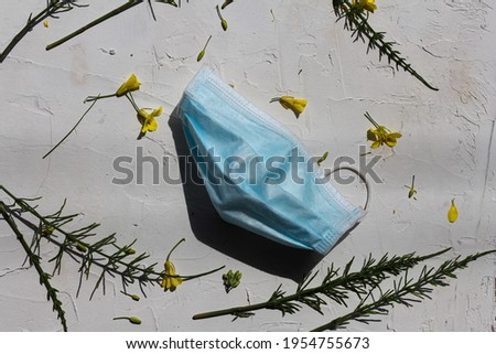 Flat lay composition of a protective medical mask. Spring and summer concept. Facial mask lying on a white background next to fresh yellow flowers and green leaves