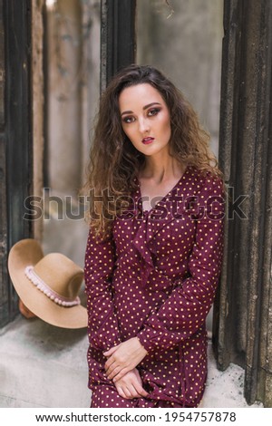 Portrait of stylish woman in a polka dot dress. Beauty. Polka dot dress. Burgundy in polka dots. Background architecture. Grey wall. Gothic architectures.