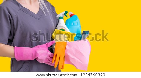 Photo of housewife in gloves holding cleanser bottles over yellow background