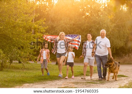 big family are walking walking american flags. Front view, american patriots on the park meadow.