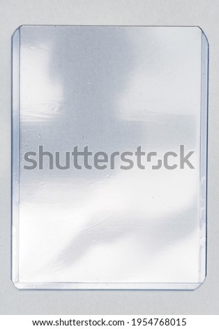 empty transparent plastic card top loader case on white paper background, gaming or trading card placeholder with nice light reflection.