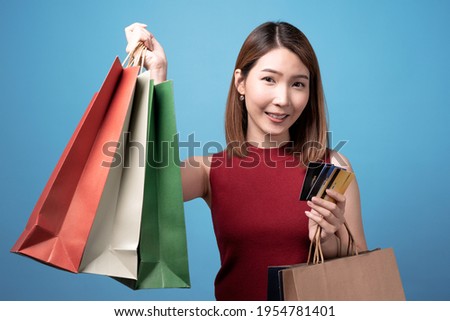 Young asian woman carrying shopping bags and credit card, Isolated on blue background.