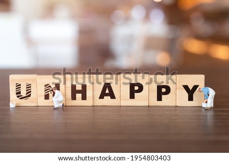 Miniature  people worker team on Unhappy word in wooden alphabet letters with prefix un crossed out, leaving the word Happy Royalty-Free Stock Photo #1954803403