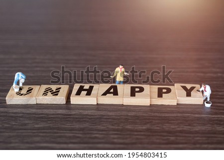 Miniature  people worker team on Unhappy word in wooden alphabet letters with prefix un crossed out, leaving the word Happy Royalty-Free Stock Photo #1954803415