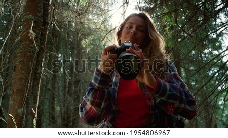 Portrait of attractive woman looking at camera. Female photographer taking photos of forest landscape on digital camera. Cheerful tourist with backpack shooting nature in summer woods