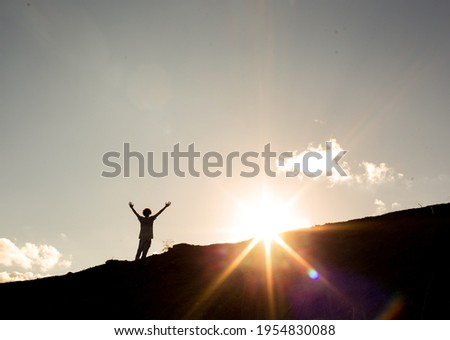 Man with arms raised after climbing a mountain, with the sun in the background. Concept of not giving up on success and dreams or freedom, success and happiness