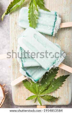 ice cream popsicle bars with coconut slices, cannabis on concrete background.